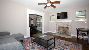 A living room with a fireplace, a ceiling fan, a television, and a dining area. - 2BR Luxury EADO House! Medical Center, Stadiums ⭐️⭐️⭐️⭐️⭐️ (Houston)