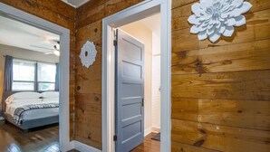 A hallway with wooden walls, a bed with a checkered blanket, and a white door. - 2BR Luxury EADO House! Medical Center, Stadiums ⭐️⭐️⭐️⭐️⭐️ (Houston)