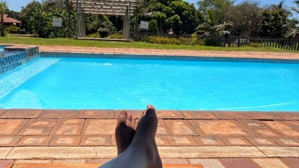 A poolside view with a clear blue sky, a wooden deck, and a pergola structure. - Zororo Lodge (Polokwane)