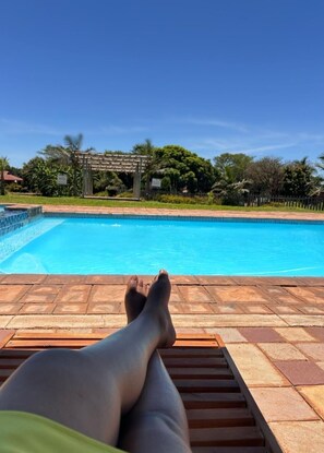 A poolside view with a clear blue sky, a wooden deck, and a pergola structure. - Zororo Lodge (Polokwane)