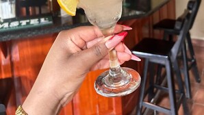 A hand holding a cocktail with a lemon slice and a straw, in a bar setting with a Miller sign in the background. - Zororo Lodge (Polokwane)