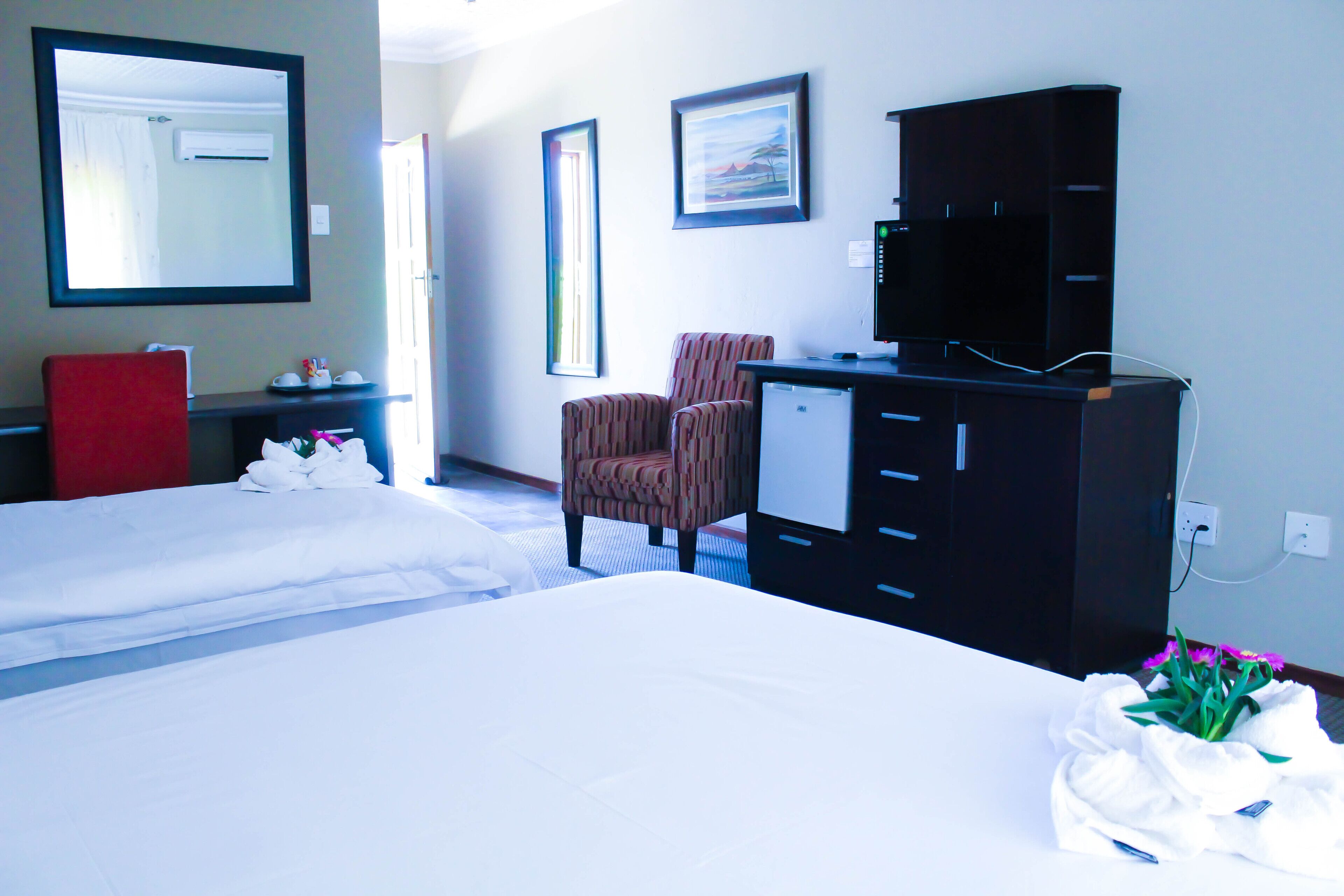 A hotel room with two beds, a desk, a chair, a wardrobe, and a mirror.