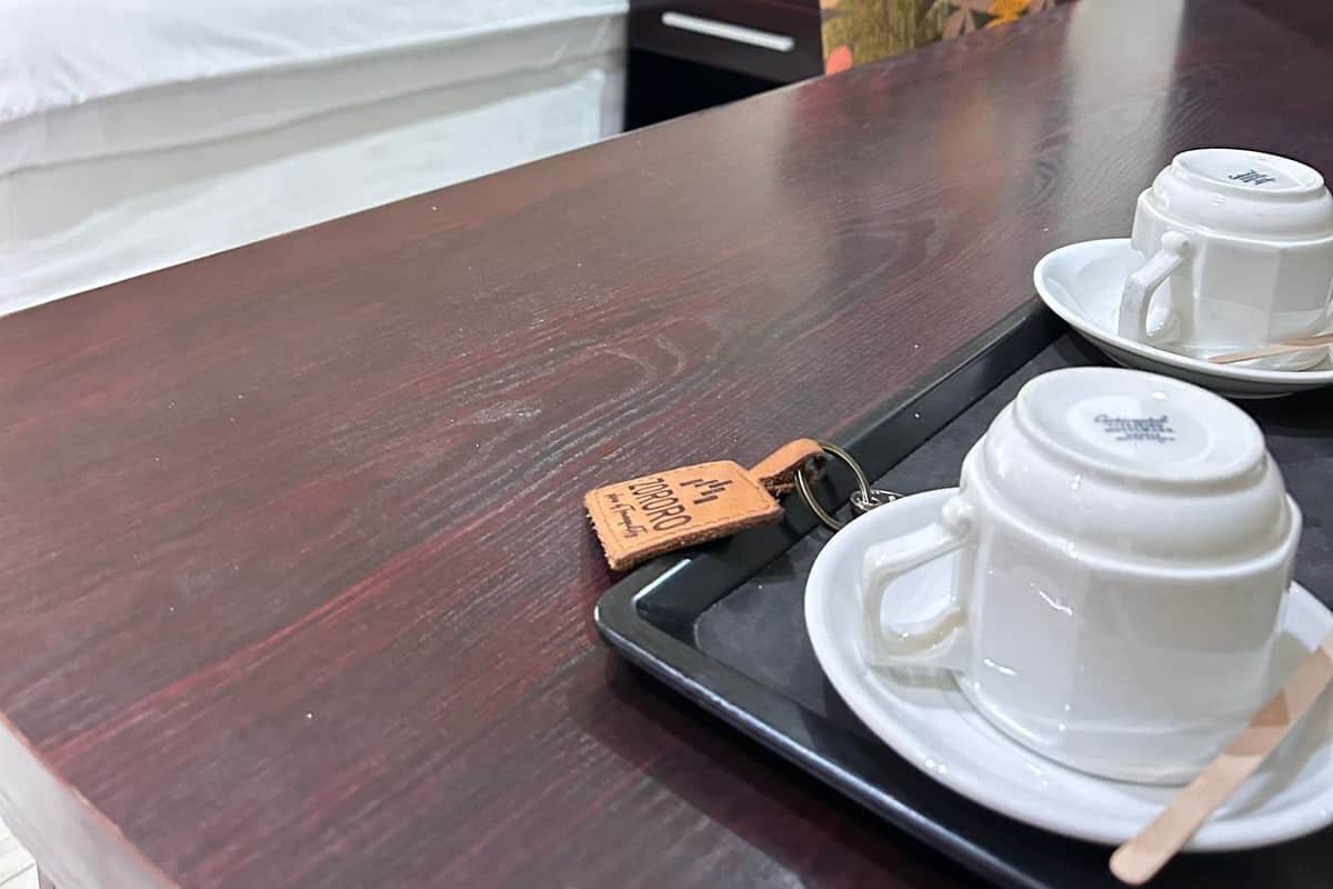 A hotel room with a neatly made bed, a floral chair, and a tray with two cups and a spoon.
