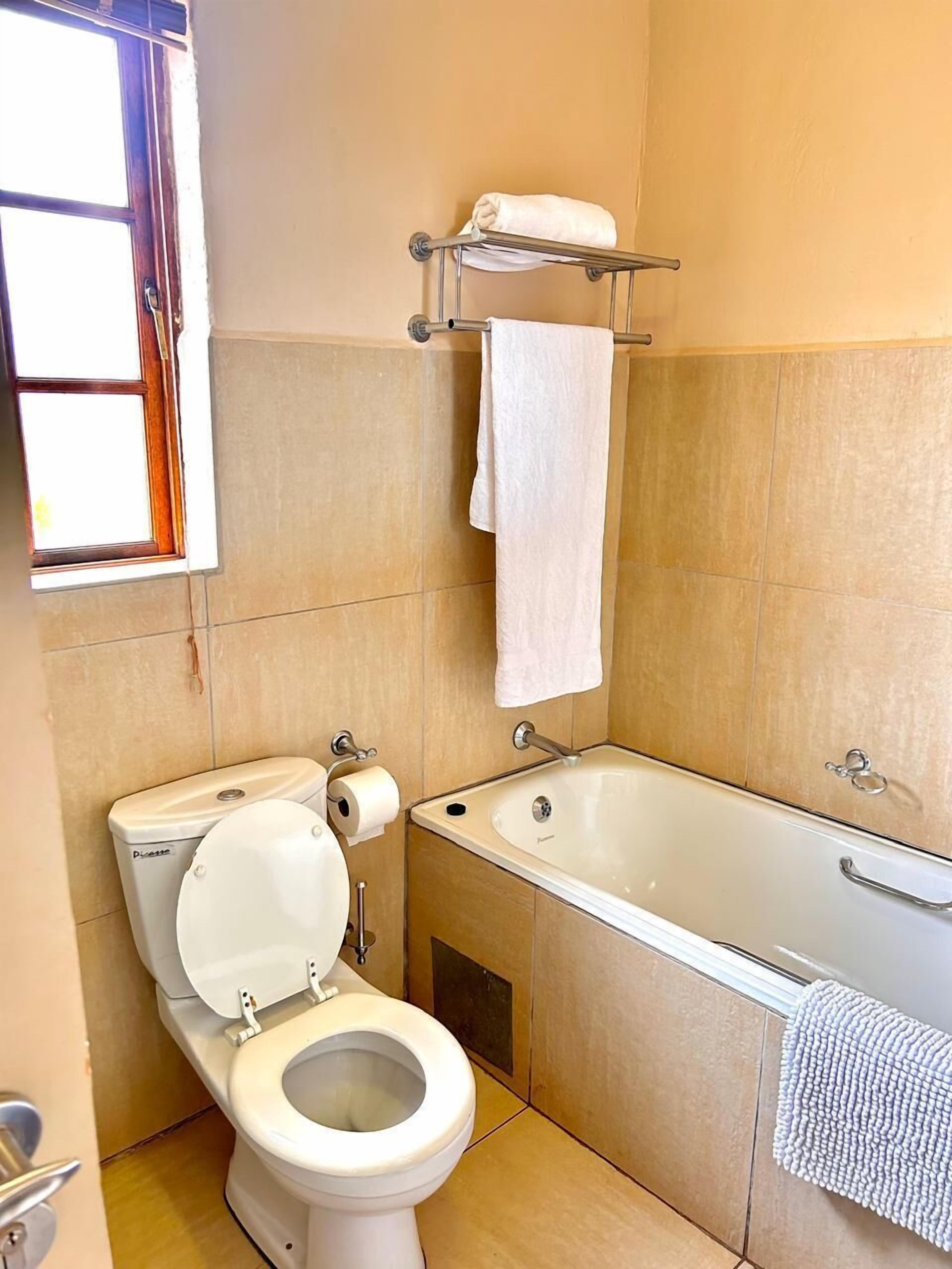 A bathroom with a toilet, sink, and bathtub. There is a towel rack above the sink and a window with blinds.