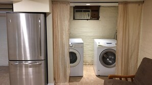 A compact laundry room with a stainless steel refrigerator, two washing machines, and a wooden chair. - 850sq. ft basement apartment in quiet area of Rock Creek Park (Washington)