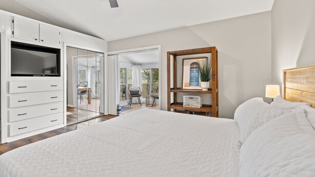 A bedroom with a large bed, a ceiling fan, a TV, and a wooden bookshelf. - Tee Time at River Club (Pawleys Island)