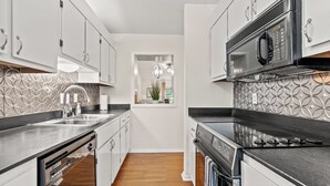 A modern kitchen with white cabinets, a black microwave, and a stainless steel dishwasher. - Tee Time at River Club (Pawleys Island)