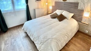 Una camera da letto con un letto, un termosifone, una finestra con tende e una parete con carta da parati decorata, oltre a una lampada fissata al muro.