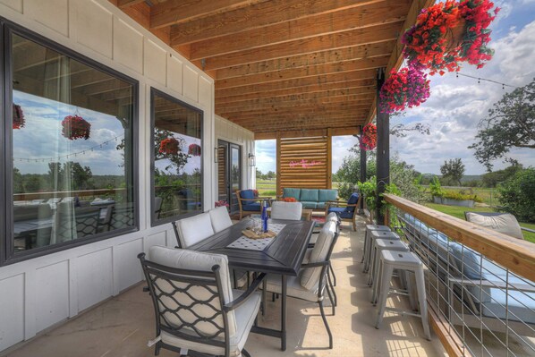 An outdoor patio with a wooden ceiling, a dining table with chairs, and hanging flower baskets.