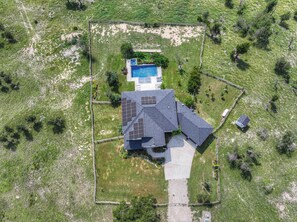 An aerial view of a house with a swimming pool, solar panels, and a fenced yard.