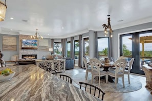 A spacious living area with a marble dining table, a fireplace, and large windows offering a view of the outdoors.