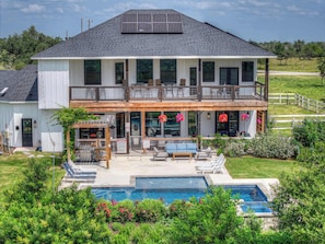 A two-story house with a large front deck, a swimming pool, and a fenced backyard.