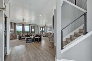 Ein geräumiges Wohnzimmer mit Treppe, großen Fenstern und einer Kristallleuchter.