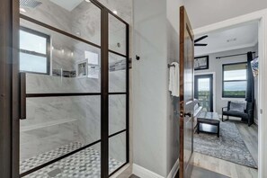 Ein modernes Badezimmer mit Duschkabine aus Glas, Marmorboden und Blick auf einen Balkon mit Sitzgelegenheit.