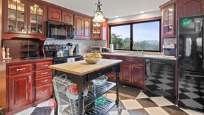 Una cocina con armarios de madera, un refrigerador negro, un ventanal grande y piso a cuadros.