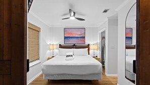 Une chambre d’hôtel avec un grand lit, deux tables de chevet avec des lampes, un ventilateur de plafond et un tableau au mur.
