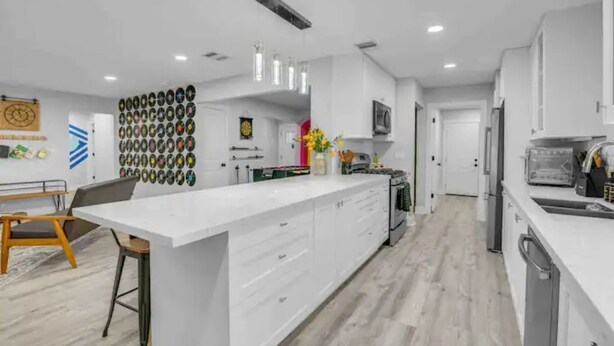 Una cocina moderna con una isla grande, armarios blancos y piso de madera.
