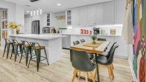 Una cocina moderna con armarios blancos, una isla central con taburetes de bar y un comedor con mesa y sillas de madera.