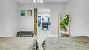 Una habitación con una cama, un banco, una planta sobre un soporte y una puerta que da a otra estancia.