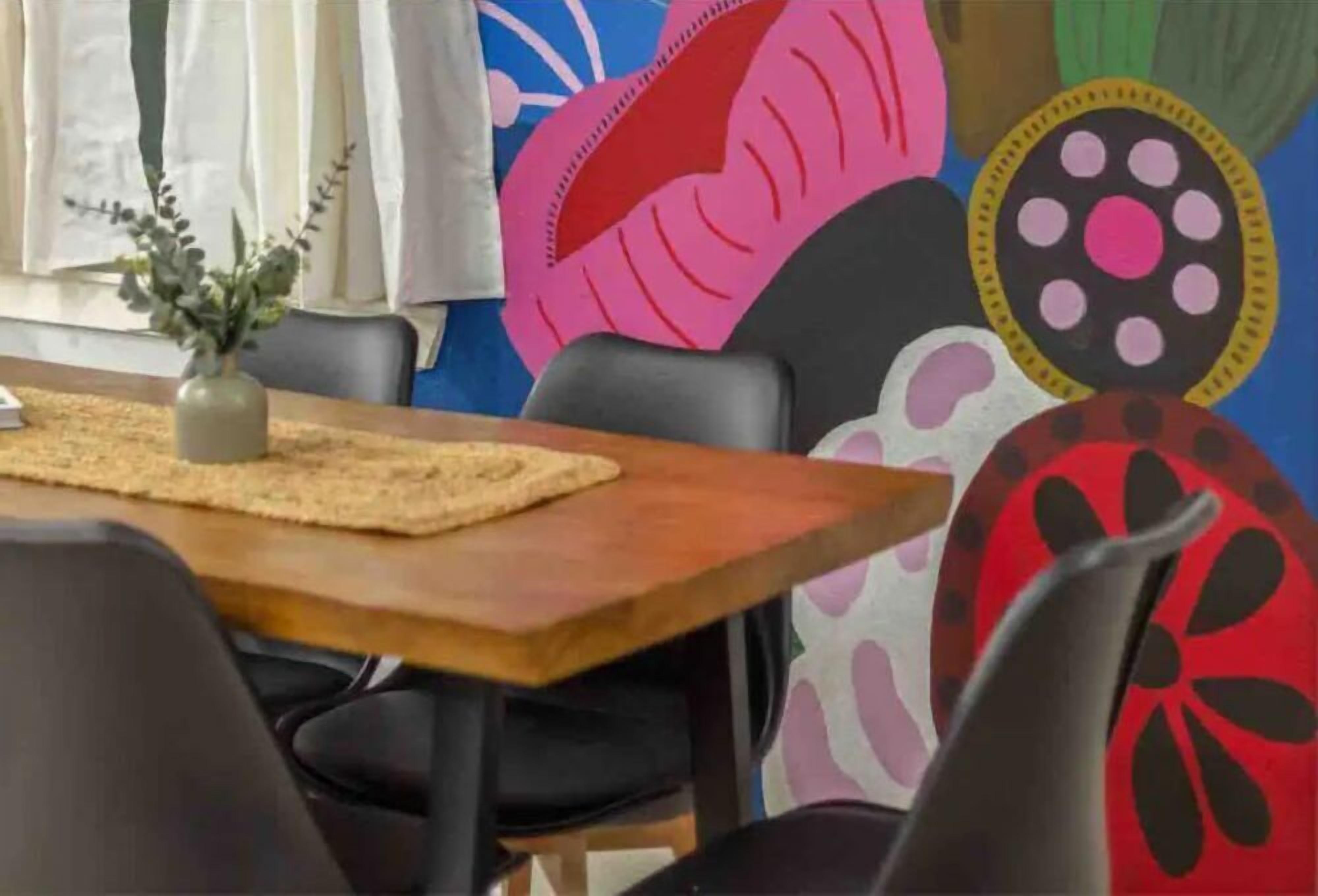 Un comedor con una mesa de madera, sillas negras y un florero con follaje.