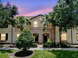 A two-story building with a symmetrical facade, a central entrance with a door, and a small balcony above the entrance. - Gorgeous 4Bd TH Pool Windsor at Westside-2018WW (Kissimmee)