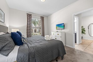 A bedroom with a bed, curtains, a TV, a dresser, and a door leading to another room. - Gorgeous 4Bd TH Pool Windsor at Westside-2018WW (Kissimmee)