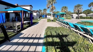 A poolside area with lounge chairs, a barbecue setup, and a building with a sign indicating an exit.