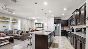 A modern kitchen with dark cabinets, a central island, and a dining area with a sofa and coffee table.