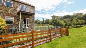 A stone building with a balcony, a wooden fence, and a grassy field with trees in the background. - Coed y Glyn Bach Equestrian (Caernarfon)