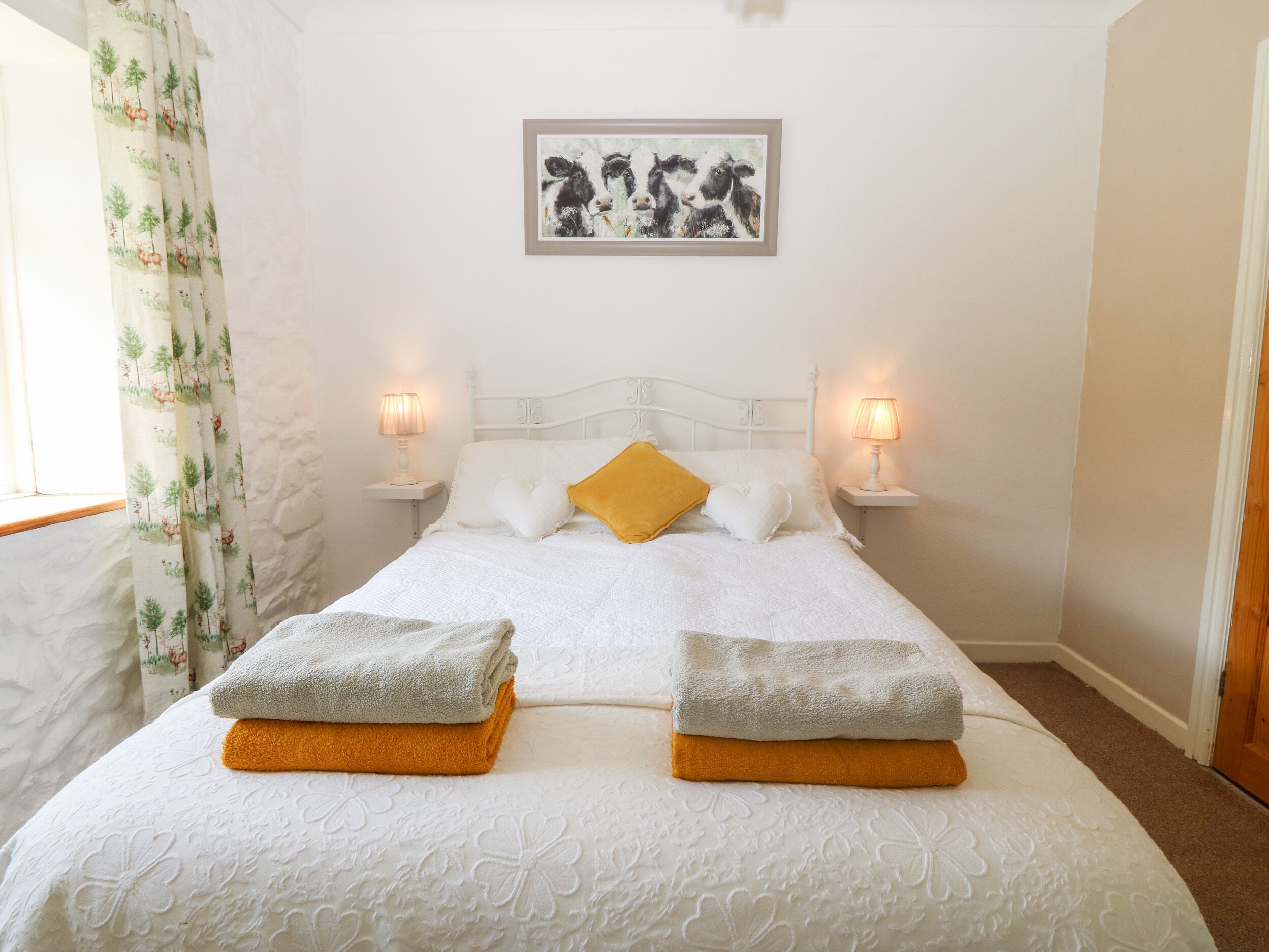 A neatly made bed with two folded towels, a white headboard, and a framed picture above it.
