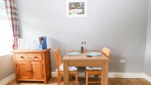 A dining area with a wooden table and chairs, a wooden cabinet, and a framed picture on the wall. - Coed y Glyn Bach Equestrian (Caernarfon)