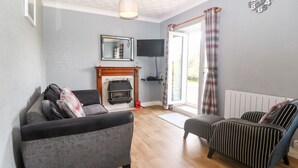 A living room with a fireplace, a sofa, a striped armchair, and a television. - Coed y Glyn Bach Equestrian (Caernarfon)