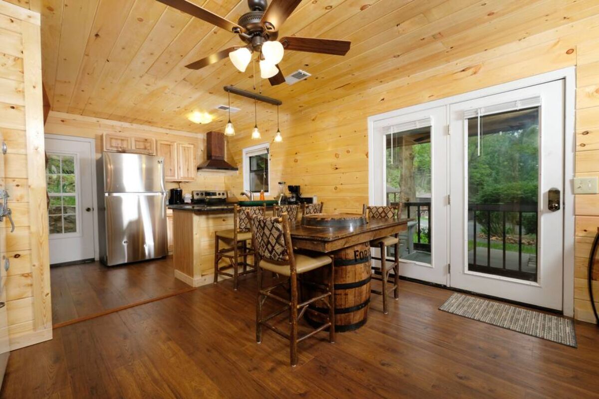 A wooden cabin interior with a kitchen, dining area, and a large window.