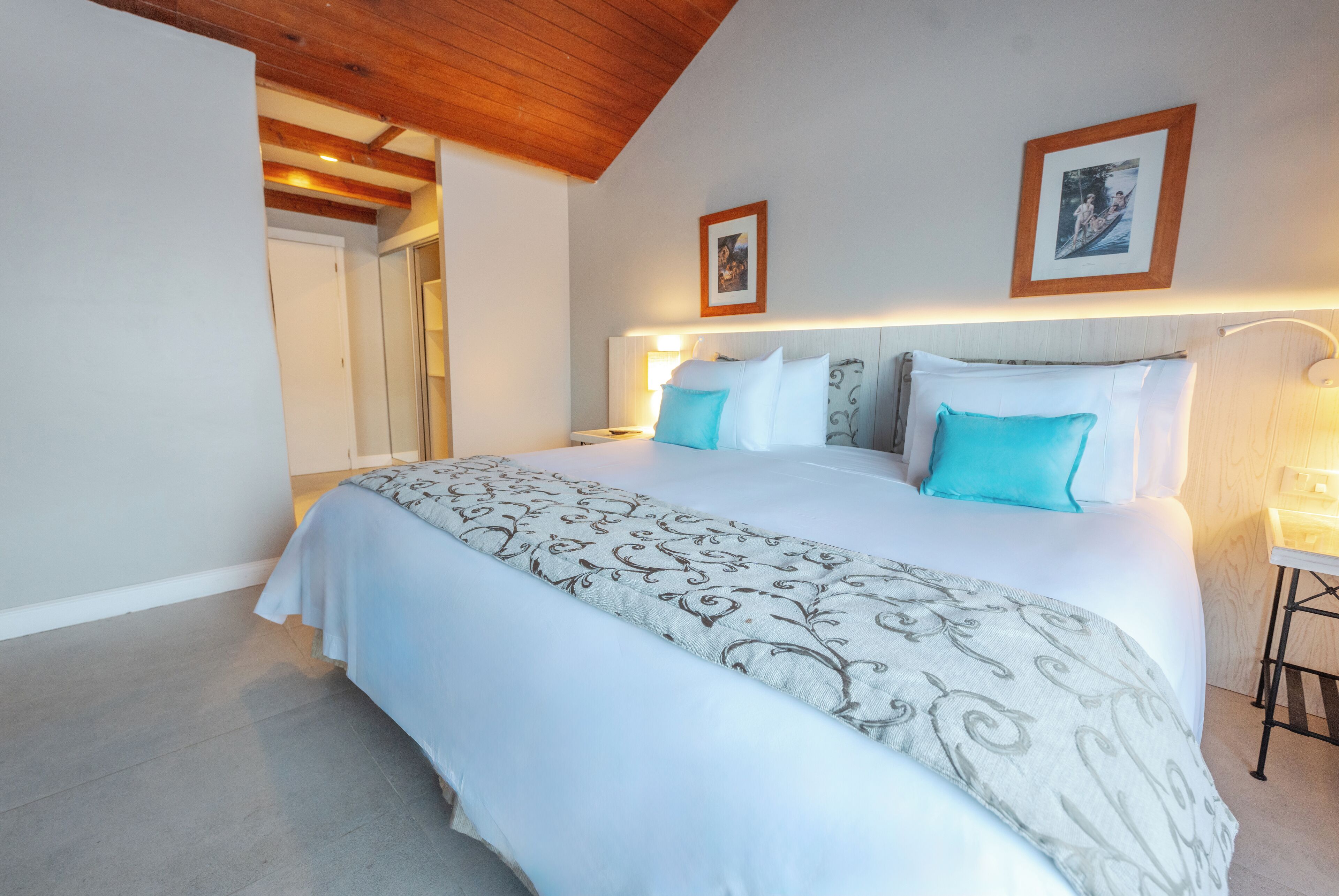 A neatly made bed with a patterned bedspread and two pillows, a wooden ceiling, and a framed picture on the wall.