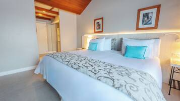 A neatly made bed with a patterned bedspread and two pillows, a wooden ceiling, and a framed picture on the wall.