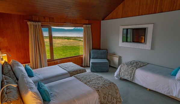 Una habitación con dos camas, una silla y una ventana con vistas a un campo y montañas.