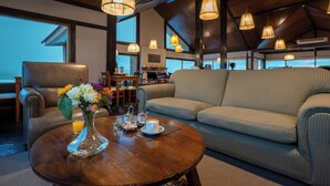 Una habitación acogedora con un sillón de cuero, un sofá, una mesa de centro de madera con un jarrón de flores y lámparas colgantes.
