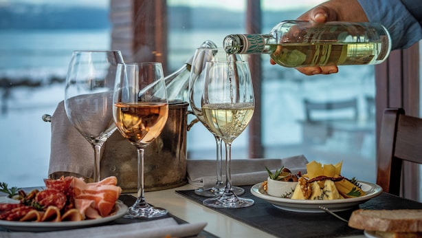 Una mesa con copas de vino, una botella sirviéndose y un plato de comida.