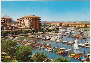 A marina with multiple boats docked, a prominent hotel building, and surrounding residential buildings. - Relax in our Seaview Flat (Caorle)