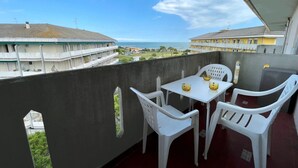 A balcony with a table and chairs, overlooking a coastal view with buildings and a clear sky. - Relax in our Seaview Flat (Caorle)
