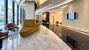 Een moderne lobby met een geel sofa, een aan de muur bevestigde televisie en een glazen ingang.