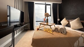 Een moderne hotelkamer met een groot bed, een flatscreen televisie, een nachtkastje met een vaas en een wijnglas, en uitzicht op de stad door het raam.