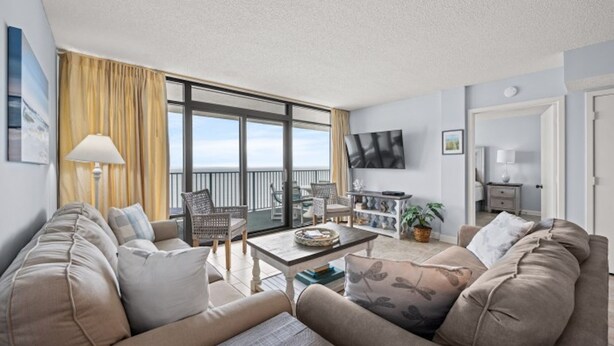 Un salon spacieux avec un grand canapé, une table basse et un balcon aménagé avec des sièges d’extérieur.