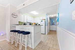Une cuisine avec des meubles blancs, un îlot central doté de tabourets et un réfrigérateur.