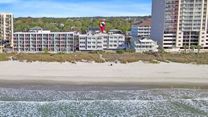 Ein Strandhotel mit mehrstöckigen Gebäuden, einem Sandstrand und einem Leuchtturm in der Ferne.