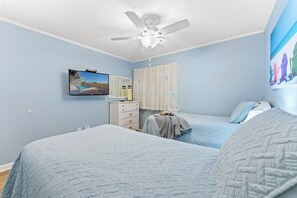 Ein Schlafzimmer mit zwei Betten, einem Deckenventilator, einem Fernseher, einem Schminktisch und einem Bild an der Wand.