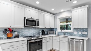 A modern kitchen with white cabinets, a stainless steel range, a microwave, and a dishwasher. - A Shore Escape! (Oak Island)