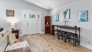 A living room with a wooden floor, a white door, a coffee table, a sofa, and a wall with framed artwork. - A Shore Escape! (Oak Island)