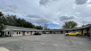 A motel with a parking lot, a yellow sports car, and a black car parked in front. - The Village Motel (Eldora)