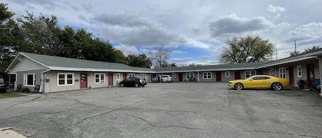 Un motel con aparcamiento, un deportivo amarillo y un coche negro estacionados al frente.